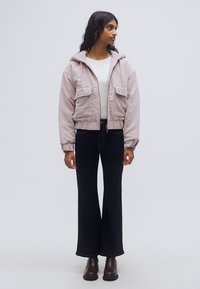 Ροζ μπουφάν με κουκούλα και υφή κοτλέ, με δύο μπροστινές τσέπες, συνδυασμένο με μαύρο καμπάνα τζιν και καφέ μποτάκια αστραγάλου. Λευκό τοπ από μέσα.