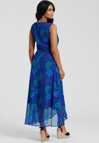 Lång, ärmlös klänning i blått med grönt blommönster. Lätt, flödande tyg. Bärs med svarta espadrillesandaler.