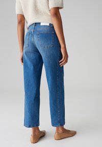 Jeans in denim blu con una vestibilità rilassata, presentano gambe dritti, tasche posteriori, cuciture visibili e orli arrotolati. Abbinati a ballerine color cammello.