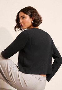 Crna rebrasta dugotrajna majica s okruglim izrezom, uparena sa svijetlosivim hlačama, koje imaju opušteni kroj i teksturirani materijal.