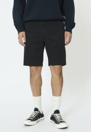 Pantaloncini neri in cotone, taglio dritto, sopra il ginocchio. Abbinati a sneakers nere e calzini bianchi, indossati con un maglione blu navy.