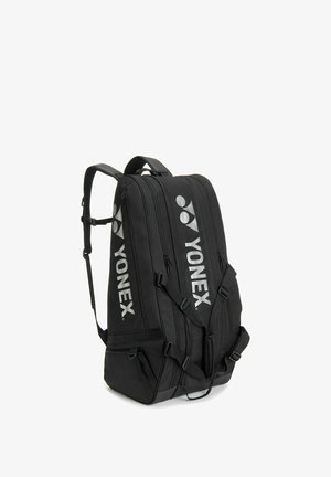 Mochila deportiva negra Yonex con múltiples compartimentos con cremallera y correas de hombro ajustables, vista en ángulo sobre fondo blanco.
