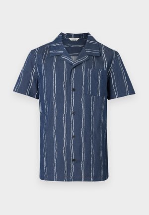 Chemise à manches courtes en tissu bleu foncé à rayures verticales blanches. Elle présente un col cranté et une poche poitrine, fermée par des boutons noirs.