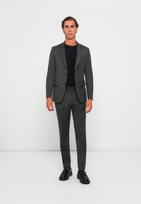 Grijs gestreept pak met een getailleerd ontwerp, een enkelgeknopte blazer, met een notch revers en bijpassende slim fit broek. Gedeeltelijk gedragen over een zwart overhemd met zwarte schoenen.