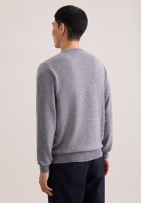 Grau gestrickter Pullover mit rundem Halsausschnitt und langen Ärmeln. Rippbündchen und Saum. Weiche Textur und lockere Passform. Von hinten gesehen.