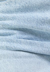 Lichtblauwe denimstof met een subtiel visgraatpatroon, met een zachte textuur en zichtbare stiksels langs de randen.