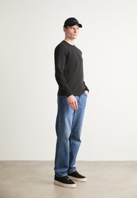 Svart langermet skjorte, blå rettbente jeans, svart caps og svarte joggesko med hvite såler. Uformell antrekk med minimal detaljering.