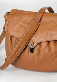 Tan leather shoulder bag with a flap, black metal clasp, and adjustable strap embossed with brand name.