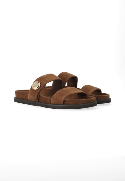 Sandali doppi con cinturino in suede marrone, suole nere e un emblema circolare dorato su un cinturino, progettati per un uso casual.