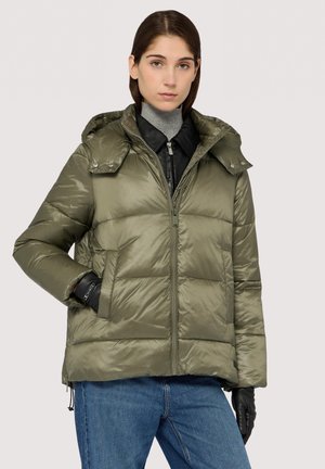 Olive green puffer jacket with a hood, featuring a front zipper, side pockets, and horizontal quilted pattern. Worn over a turtleneck.