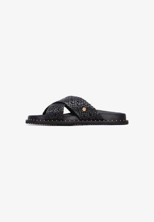 Sandalias de cuero negro trenzado con diseño de correas cruzadas, con una suela plana adornada con tachuelas doradas en el borde.