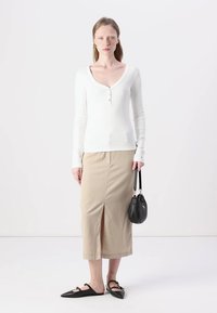 White long-sleeve top with a V-neck and button details, paired with a beige midi skirt featuring a front slit, and black flat shoes.