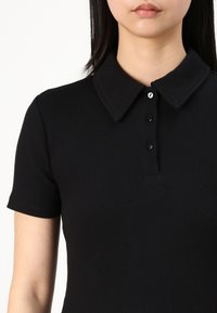 Svart ribbad polo skjorta med klassisk krage, korta ärmar och en treknappsknäppning med svarta knappar för en stilren finish.