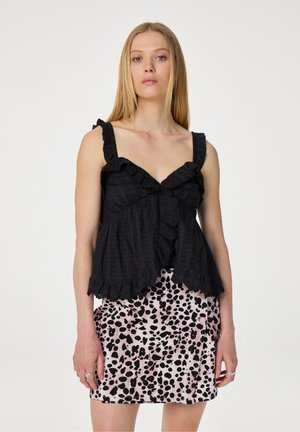 Zwarte top met franje en textuurontwerp, en een roze rok met een zwart stippenpatroon. Beide kledingstukken hebben een losse pasvorm.