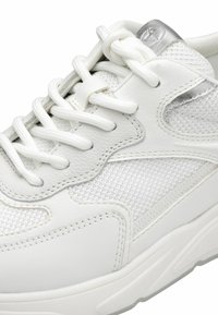 Sneaker bianco con una combinazione di pelle liscia e mesh testurizzato, con lacci bianchi, dettagli in argento e una suola spessa e ammortizzata.