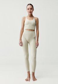 Béžová souprava sportovní podprsenky a legín vyrobená z elastické tkaniny, s ribbenou strukturou a přiléhavým designem se švy.