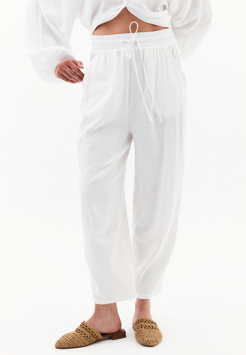Witte, lichte linnen broeken met een elastische tailleband en trekkoord. Voorzien van zijzakken en een relaxte pasvorm. Gecombineerd met geweven, beige muiltjes.