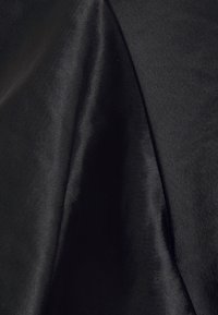 Tissu noir drapé pour mettre en valeur une texture lisse et légèrement brillante, avec des variations de lumière créant des reflets subtils et des effets d'ombre.