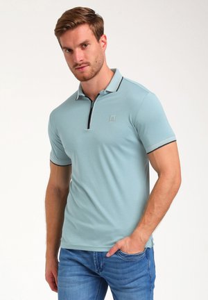 Kortærmet polo-shirt i lyseblå, med lynlås i kraven, kontrastkanter og et diskret logo på brystet. Glat stofstruktur.