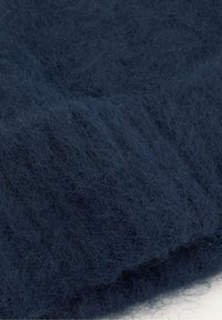 Tmavě modrá měkká chlupatá tkanina s pletenou strukturou, ukazující jemné vlákna a žebrovaný vzor.