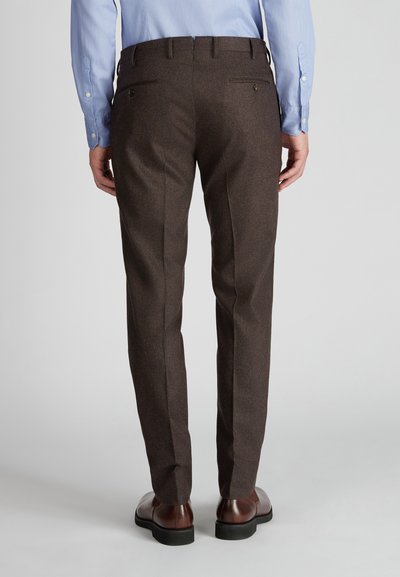 Braune Wollhosen mit strukturiertem Finish, schmaler Schnitt und Gesäßtaschen mit Knöpfen. Kombiniert mit braunen Lederschuhen.