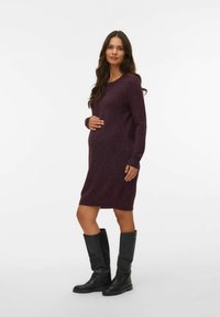 Robe de maternité tricotée de couleur baie avec des manches longues, un col rond et une silhouette ajustée, associée à des bottes noires jusqu'aux genoux.