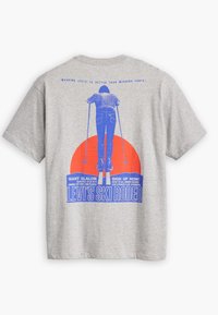 Camiseta de algodón gris con un gráfico azul y rojo en la parte posterior, que representa a un esquiador con texto sobre un evento de esquí y detalles de patrocinio.