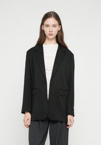 Čierne sako s tenkými pásikmi, zapínanie na jeden gombík, výstrih so zárezmi a predné vrecká. Nosené cez biele tričko. Mäkká textúra látky.