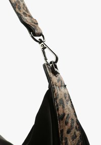 Cinghia della borsa nera con un design a stampa leopardata, dettaglio in metallo argentato lucido, che mostra trame di pelliccia sintetica e pelle liscia.