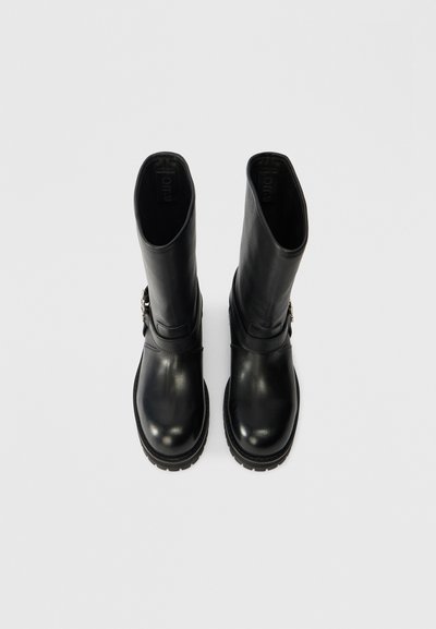 Μαύρες δερμάτινες μπότες αστραγάλου με φαρδύ κορμό, υφασμάτινη σόλα και λεπτομέρεια λουριού με μεταλλική λεπτομέρεια. Λείος επιφανειακός σχεδιασμός στο σύνολό του.