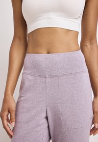Lichtpaarse sportbroek met een brede tailleband, een gladde textuur en zijzakken. Gemaakt in combinatie met een wit aansluitend shirt.