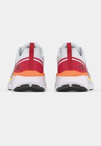 Sportcipők, fehér hálós felsőrésszel, piros részletekkel, narancs és sárga talppal, texturált gumitalppal és húzófüllel a saroknál.