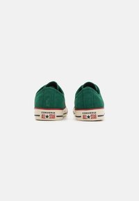 Vihreät matalavartiset Converse All Star -lenkkarit näkyvät selkäpuolelta valkoista taustaa vasten.