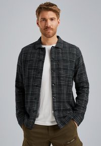 Camisa de botones en diseño de cuadros en negro y gris, con cuello, mangas largas y tejido texturizado. Llevada sobre una camiseta blanca.