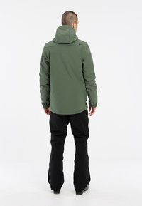 Grøn vandtæt jakke med hætte, der har elastiske manchetter, lige snit og sorte bukser. Minimalistisk design, blød tekstur og glat finish.