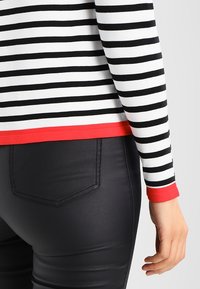 Zwart-wit gestreepte longsleeve top met een rode accentrand aan de zoom, gecombineerd met zwart, aansluitende broek van een gladde stof, die de elegante, soepele texturen benadrukt.