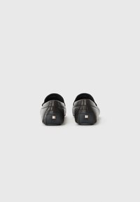 Pantofi slip-on din piele neagră cu un finisaj texturat, vârf rotunjit și toc mic pătrat cu un accent metallic. Design neted și minimalist.