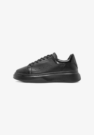 Zwarte leren sneaker met een matte afwerking, ronde neus, gestikte details en een dikke zwarte rubberen zool. Veters lopen door een geperforeerde bovenkant.