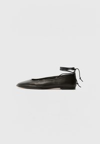 Bailarinas de couro preto com bico fino, laço no tornozelo e sola plana, apresentando uma textura suave e um design minimalista.
