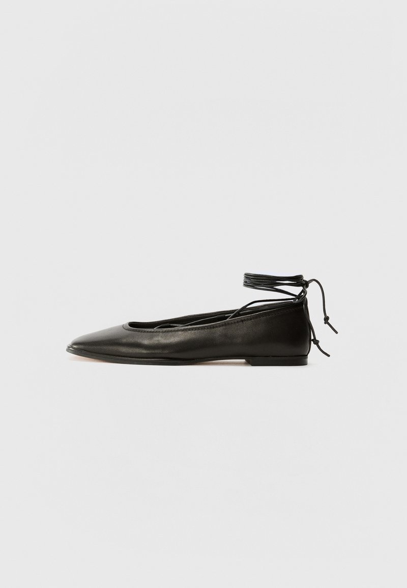 Bailarinas de couro preto com bico fino, laço no tornozelo e sola plana, apresentando uma textura suave e um design minimalista.
