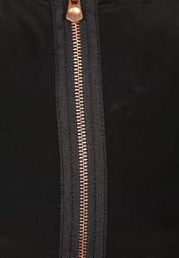 Svart tyg med en central koppardragkedja. Dragkedjan har ett metallhandtag och ett strukturerat band längs med tänderna, vilket framhäver dess funktionalitet.