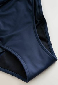 Tamsiai mėlyni ir juodi aukštu liemeniu maudymosi kostiumėlio apačia iš lygaus audinio su detaliu siuvimu ant šviesaus paviršiaus.