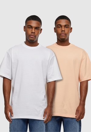 Twee T-shirts met korte mouwen: een witte en een perzikkleurige. Beide hebben een losse pasvorm, ronde halslijnen en een zachte, gladde katoenstructuur.