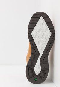 Talpă din cauciuc maro cu intermediar alb, având un model texturat și un accent verde. Vedere laterală a unei cizme Timberland.