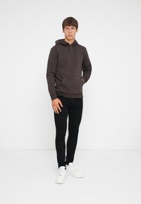 Dark brown hoodie with a kangaroo pocket, drawstring hood, and ribbed cuffs, paired with black skinny jeans and white sneakers.