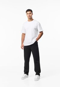 Bílé bavlněné tričko, volný střih, krátké rukávy; v kombinaci s černými tepláky, měkká textura; doplněno bílými teniskami.