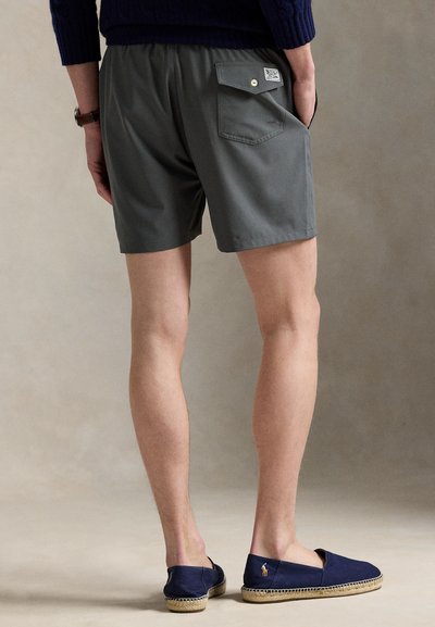 Pilkos šortai su elastinga juosmens juosta, galinėje kišenėje sagos užsegimas, derinami su tamsiai mėlynais espadriliais. Lygus, lengvas audinys.