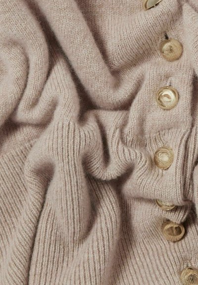 Tejido de punto rosa claro con textura de canalé, que presenta grandes botones redondos a lo largo del lado derecho, creando una apariencia acogedora y en capas.