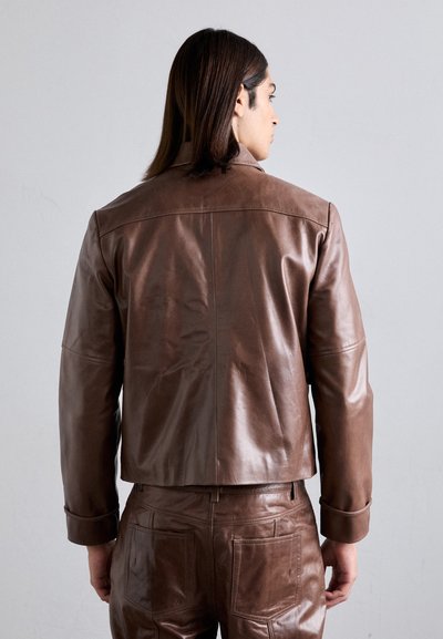 Giacca in pelle marrone con design corto, caratterizzata da una texture liscia e maniche con bottoni. Accompagnata da pantaloni in pelle marrone coordinati.