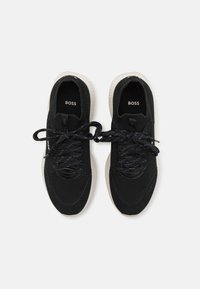 Černé tenisky z materiálů mesh a semiš, s texturovaným povrchem, kulatou špičkou a kontrastní bílou gumovou podešví. Šňůrky jsou tmavé.